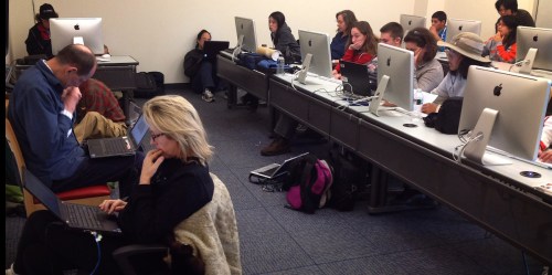 A classroom filled with students working on laptops at desks with iMac computers.
