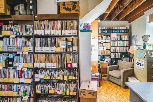 A cozy office space filled with shelves of organized files, boxes, and a comfortable chair in the corner.