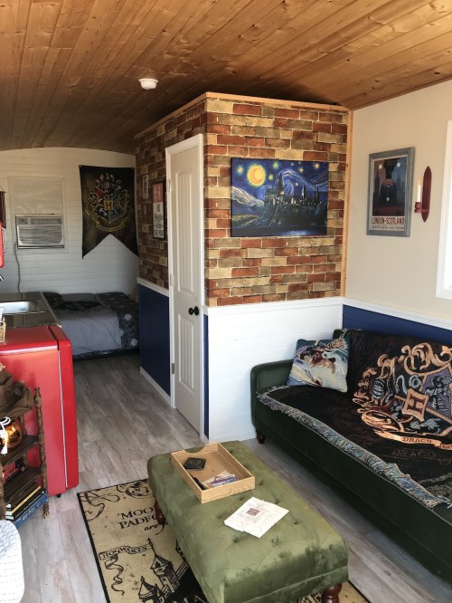 Cozy interior of a small home featuring a brick accent wall, a green ottoman, and themed decor.