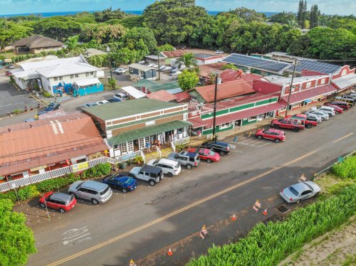 Aerial view of a colorful row of shops along a street, with parked cars and lush greenery in the background.
