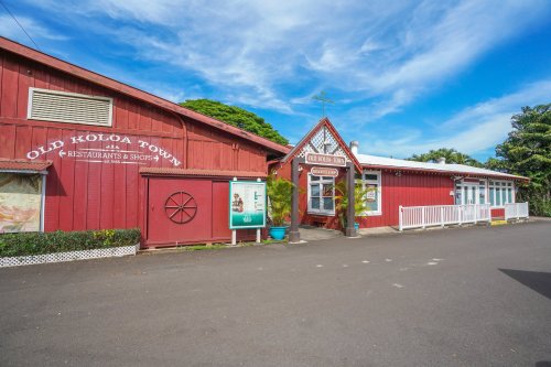 Historic red buildings of Old Koloa Town, featuring shops and restaurants, under a bright blue sky.
