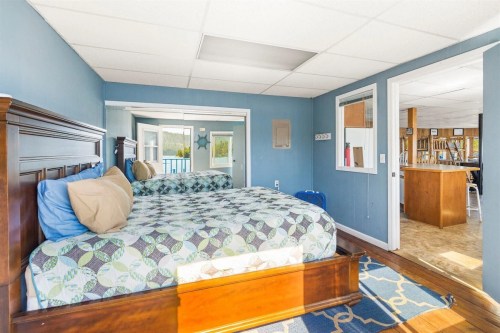 A cozy bedroom with two beds, blue walls, and a view of a kitchen area through an open doorway.