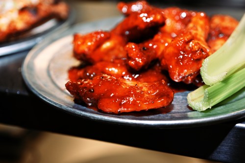 A close-up of a plate with glazed chicken wings and celery sticks.