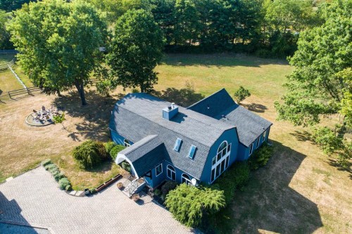 Aerial view of a blue house surrounded by trees and a grassy area, with a circular fire pit nearby.