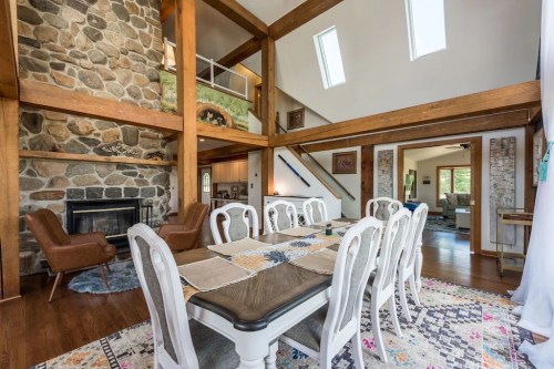 A spacious dining area with a wooden table, stone fireplace, and large windows, featuring rustic decor and natural light.