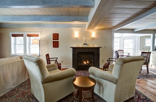 Cozy living room with two armchairs, a small table, a fireplace, and a view of a bright kitchen area.