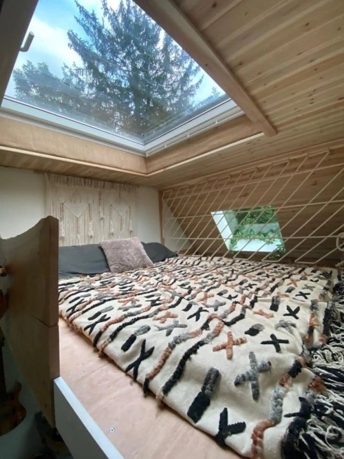 Cozy loft bedroom with a skylight, wooden walls, and a patterned blanket on a bed.