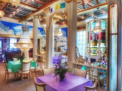 Brightly decorated restaurant interior with colorful tables, chandeliers, and vibrant wall murals.