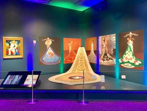 Art exhibit featuring colorful dresses and paintings, with a central display of a gown and illuminated walls.