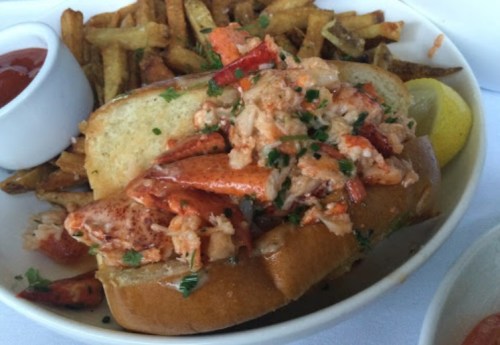A lobster roll topped with lobster meat, served with fries and a side of ketchup.