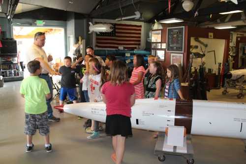 A group of children listens to a guide near a missile display in a museum setting.