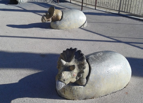 Two stone sculptures resembling lions partially embedded in the ground, set against a textured surface.