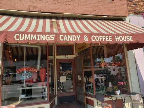 Exterior of Cummings' Candy & Coffee House, featuring a striped awning and large windows displaying candy and coffee signs.