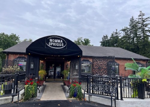Exterior of Momma Spriggs restaurant, featuring a black awning, brick facade, and colorful flower arrangements.