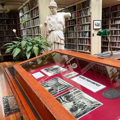 A library display case with historical photos, a statue, and bookshelves in the background.