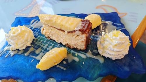 A slice of lemon cheesecake on a blue plate, garnished with whipped cream and lemon slices.