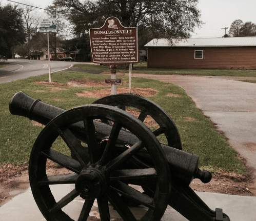 A cannon on display in Donaldsonville, Louisiana, with a historical marker in the background.