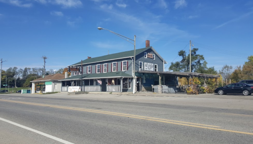 A two-story building with a green roof, featuring a porch and signage, set along a road under a clear blue sky.