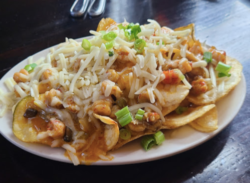 A plate of nachos topped with cheese, shrimp, and green onions on a wooden table.