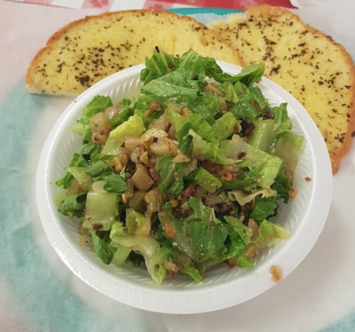 A bowl of chopped salad with lettuce, vegetables, and nuts, accompanied by two slices of herb garlic bread.