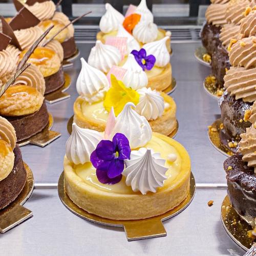 A display of colorful mini cakes topped with meringue, flowers, and decorative elements in a pastry shop.