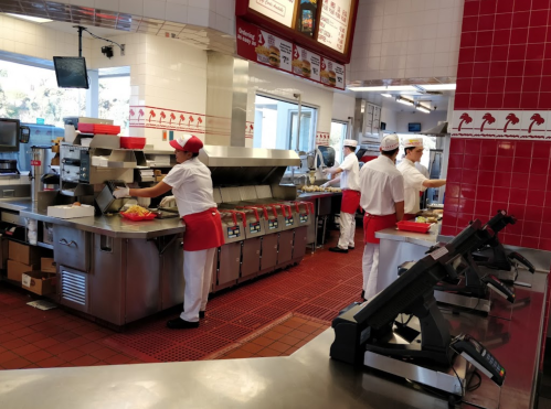 A busy fast-food kitchen with staff in uniforms preparing food and taking orders at the counter.