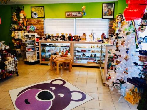 A colorful gift shop featuring shelves of toys, a white Christmas tree, and a bear-themed rug on the floor.