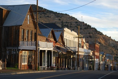 A historic street lined with wooden buildings and storefronts, set against a backdrop of rolling hills.