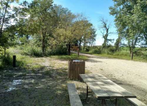 A gravel path leads into a wooded area, with a picnic table and a signpost visible in the background.