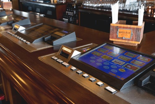 Close-up of a bar counter with electronic gaming machines and a wooden holder for straws.