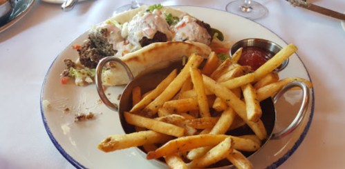 A plate with a sandwich filled with meat and toppings, accompanied by a side of crispy French fries.