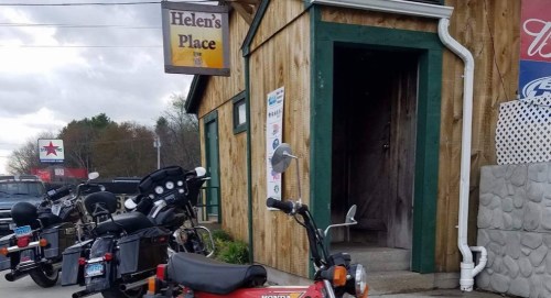 A rustic wooden building with a sign reading "Helen's Place" and parked motorcycles in front.