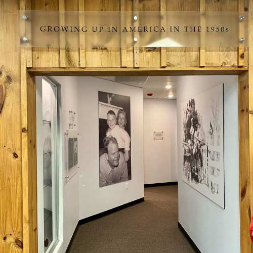 Entrance to an exhibit titled "Growing Up in America in the 1950s," featuring a wooden frame and white walls.