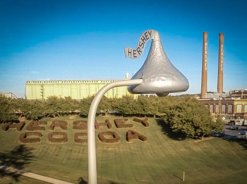 A large Hershey's Kiss sculpture stands in front of the Hershey Chocolate factory, with "Hershey Cocoa" in the landscape.