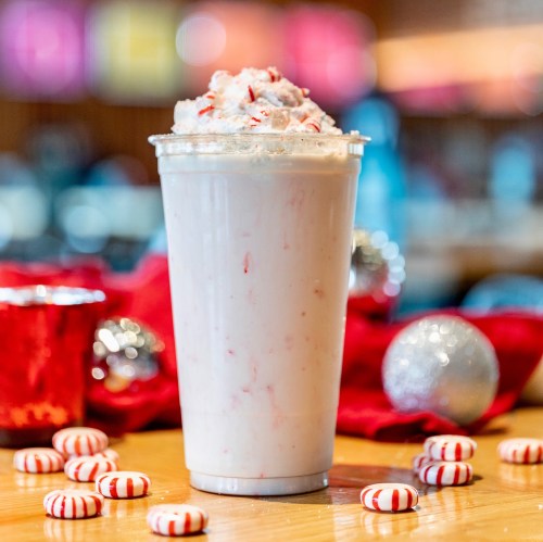 A festive peppermint milkshake topped with whipped cream, surrounded by candy canes and holiday decorations.