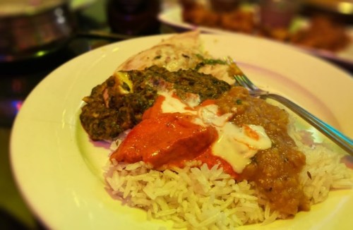A plate of rice topped with green curry, red sauce, and lentils, accompanied by a piece of flatbread.