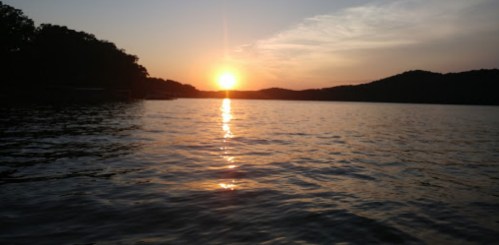 A serene sunset over a calm lake, with mountains silhouetted against the colorful sky.