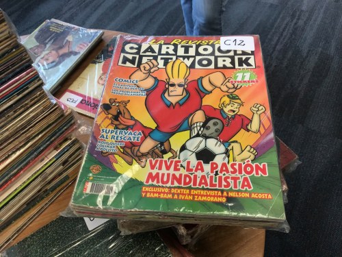 A colorful magazine featuring Cartoon Network characters, with a soccer theme and stickers, on a table of magazines.