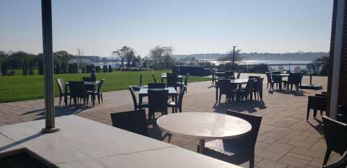 Outdoor seating area with tables and chairs overlooking a serene lake and clear blue sky.