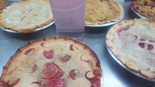 A variety of pies on display, including a strawberry pie with a heart pattern and a crumb-topped pie in the background.