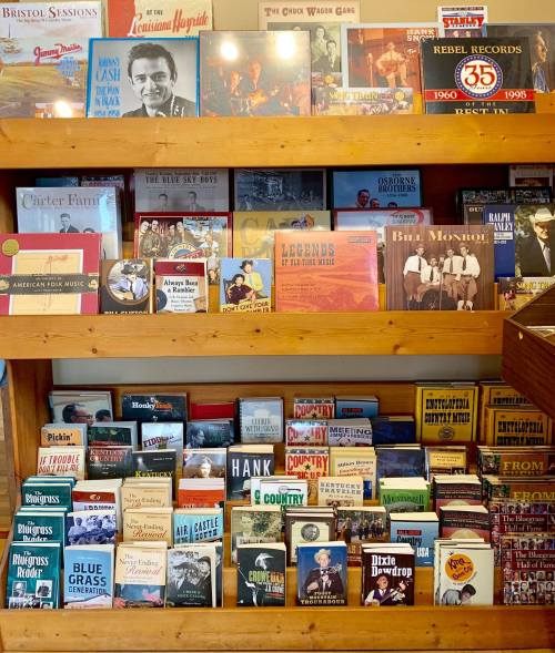 A wooden shelf filled with various music albums and books, showcasing country and bluegrass artists and history.
