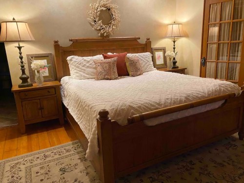 Cozy bedroom featuring a wooden bed, decorative pillows, two lamps, and a floral wreath on the wall.
