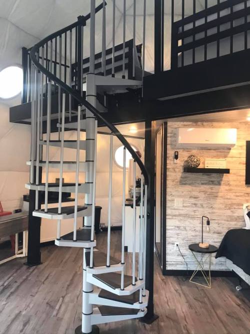 A modern spiral staircase leads to a loft in a stylish interior with circular windows and wooden accents.