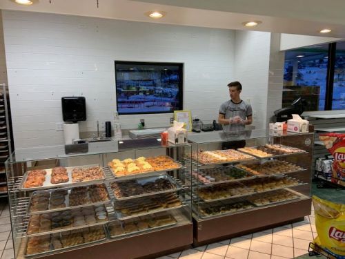 A bakery display case filled with various pastries and a young employee standing behind the counter.