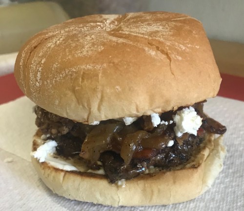 A close-up of a hamburger with a soft bun, ground beef patty, sautéed onions, and crumbled cheese.