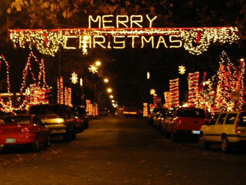 A festive street adorned with colorful Christmas lights and a "Merry Christmas" sign overhead.