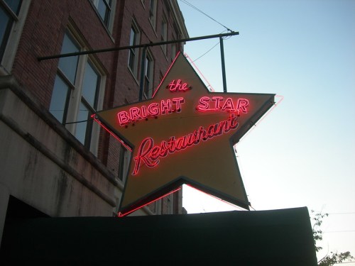 Neon sign of "The Bright Star Restaurant" in a star shape, glowing against a twilight sky.