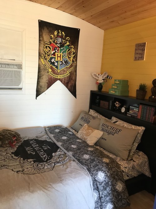 Cozy bedroom featuring a Hogwarts banner, themed bedding, and a bookshelf with decorative items.