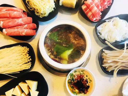 A hot pot surrounded by various ingredients like noodles, vegetables, and sliced meats on black plates.