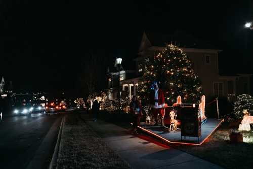 A festive street scene at night, featuring a decorated house with a Christmas tree and colorful lights.